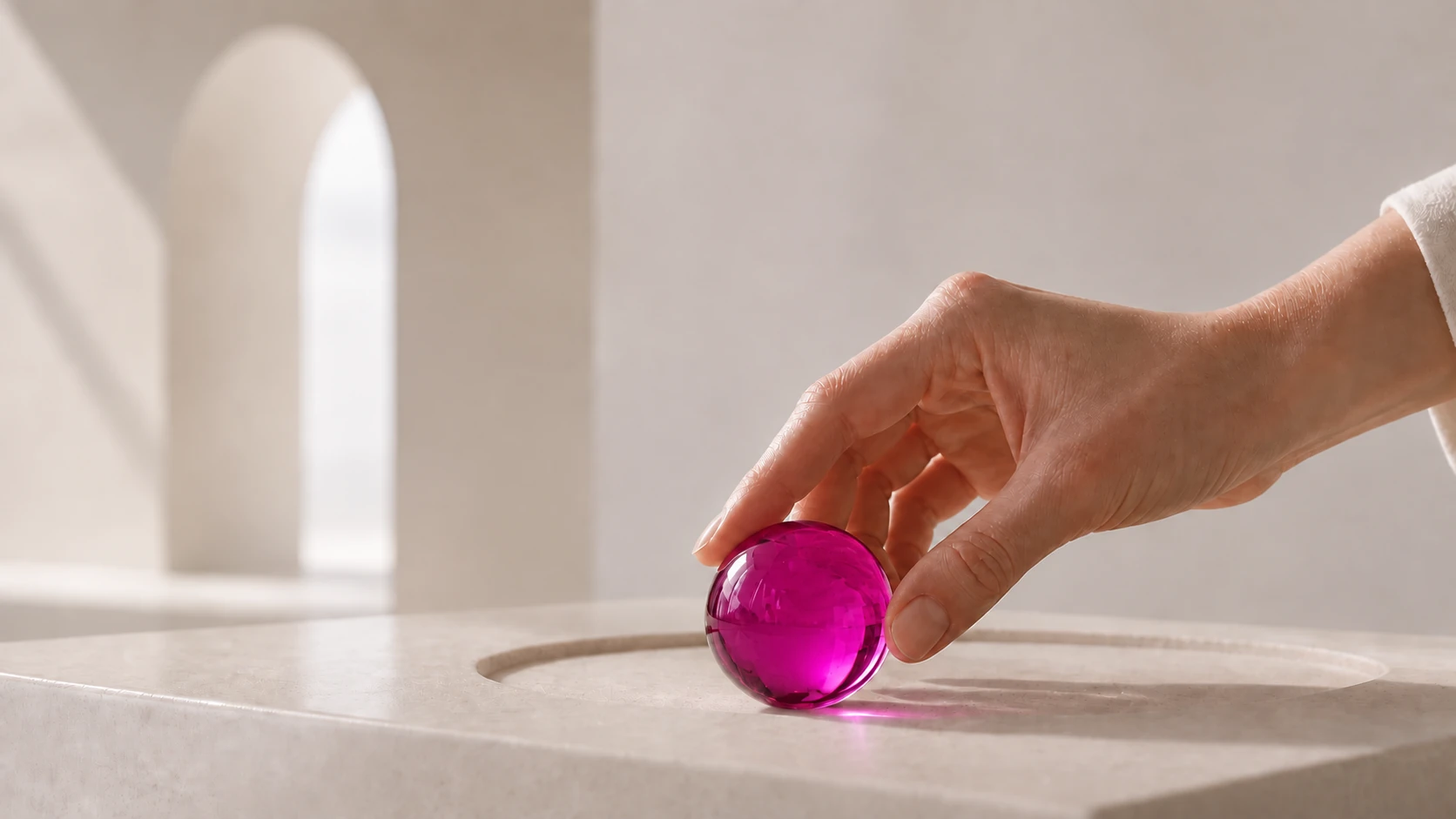 En hand placerar en genomskinlig magenta glaskula i ett avgränsat spår på en ljus stenyta.